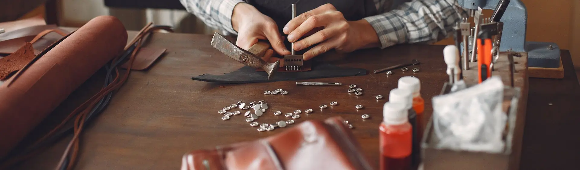 Artesano de mandil trabajando una pieza de cuero con martillo sobre su banco de taller
