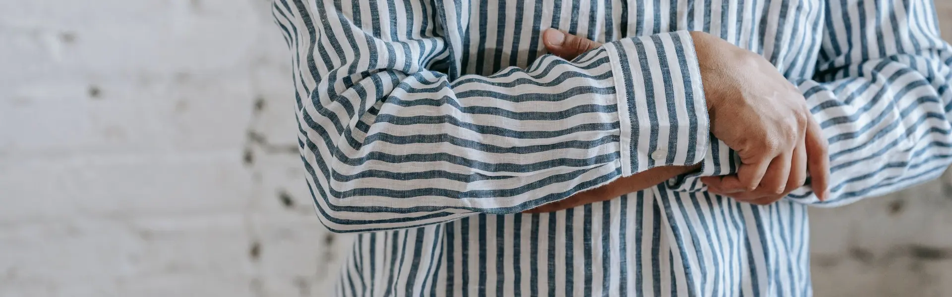 Detalle de una camisa de lino de raya azul sobre blanco, con la manga vuelta sobre el antebrazo