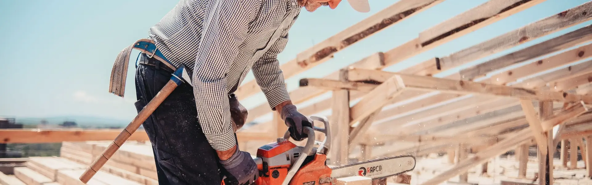 Carpintero veterano cortando listones con la motosierra sobre la estructura de madera de una cubierta en obra