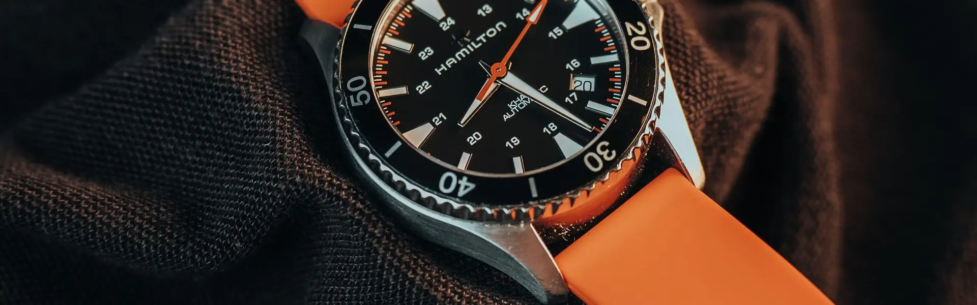 Reloj de buceo de esfera negra y bisel giratorio montado sobre una correa de caucho naranja, con gotas de agua