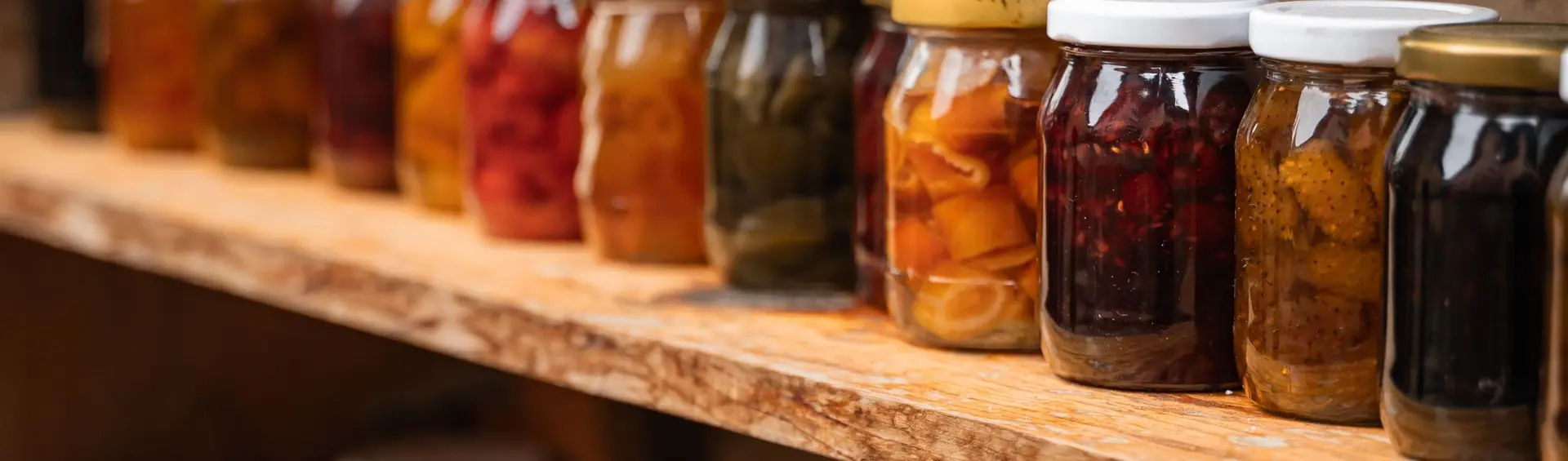 Tarros de conserva casera de frutas y hortalizas, sin etiquetas, alineados sobre una balda de madera rústica