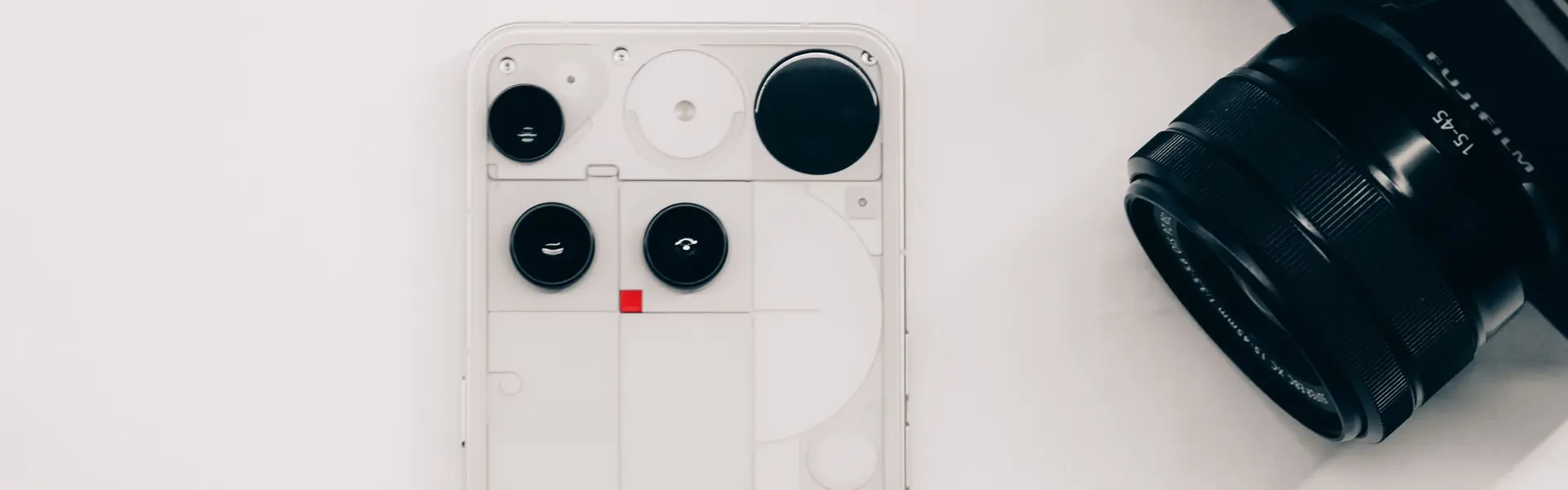Teléfono de carcasa transparente, objetivo fotográfico y cargador dispuestos sobre fondo blanco