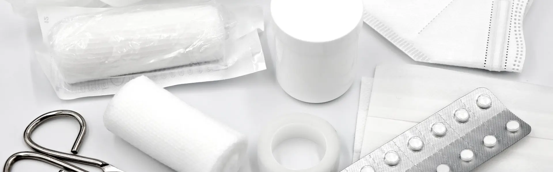 Contenido de un botiquín dispuesto sobre fondo blanco: vendas, guantes, mascarilla, tijeras, esparadrapo y comprimidos