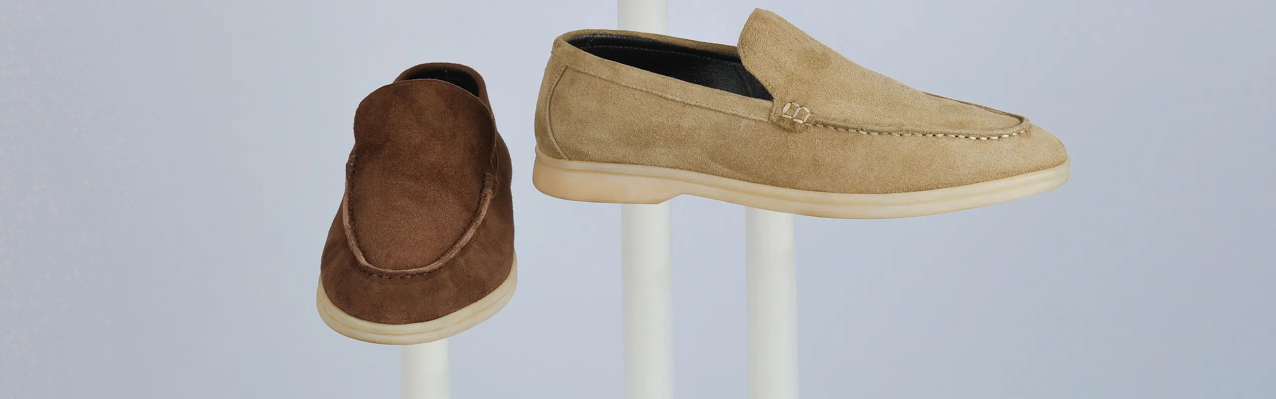 Dos mocasines de ante, beige y chocolate, expuestos sobre pedestales blancos