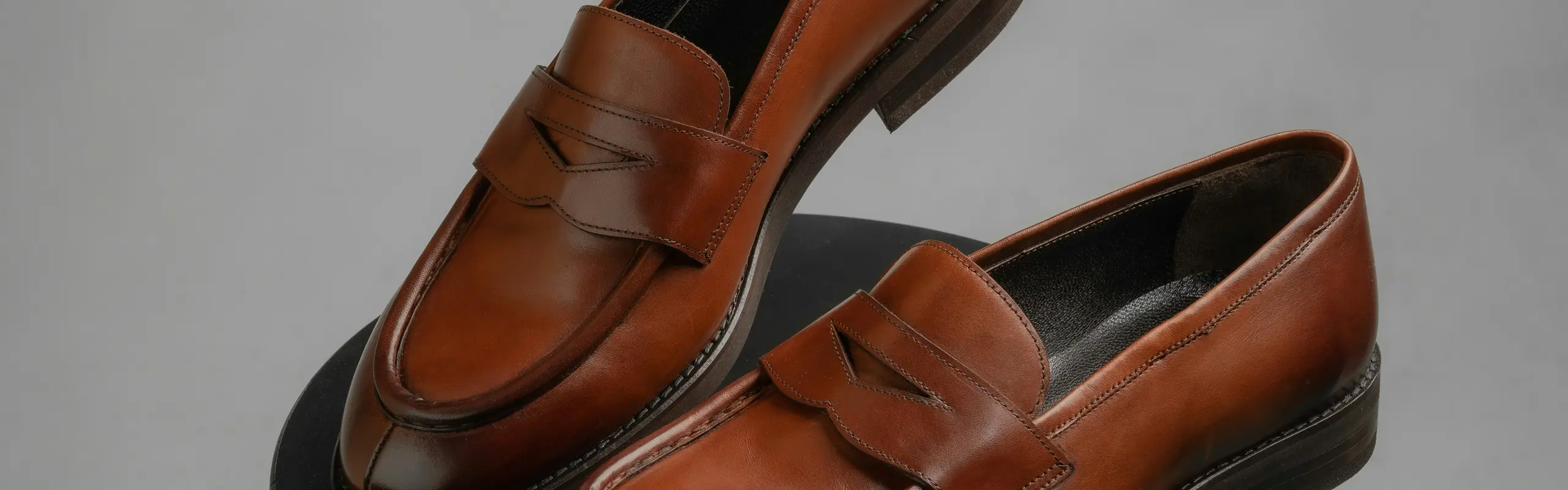 Mocasines penny de piel bruñida color coñac sobre un taburete negro