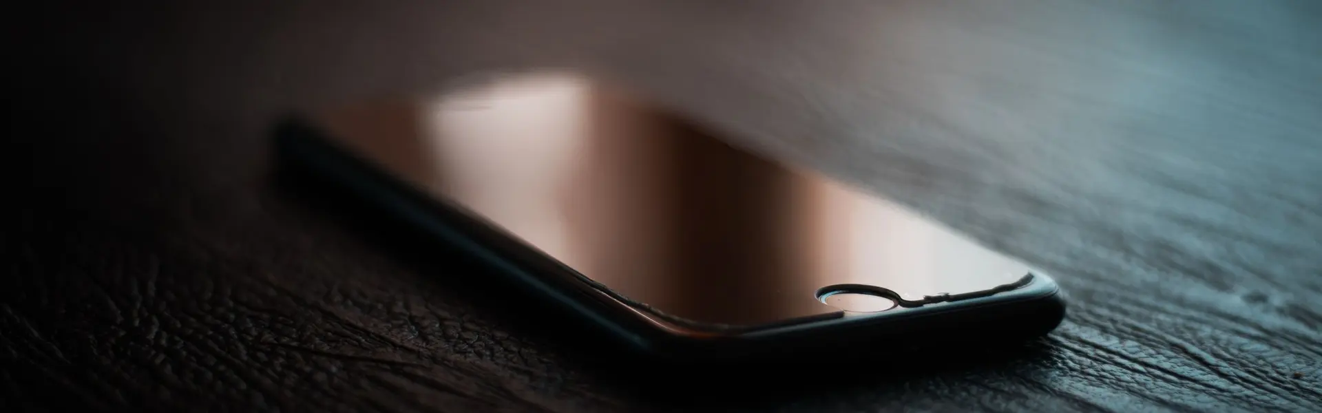 Teléfono con la pantalla apagada sobre una mesa de cuero oscuro, iluminada por la última luz de la tarde