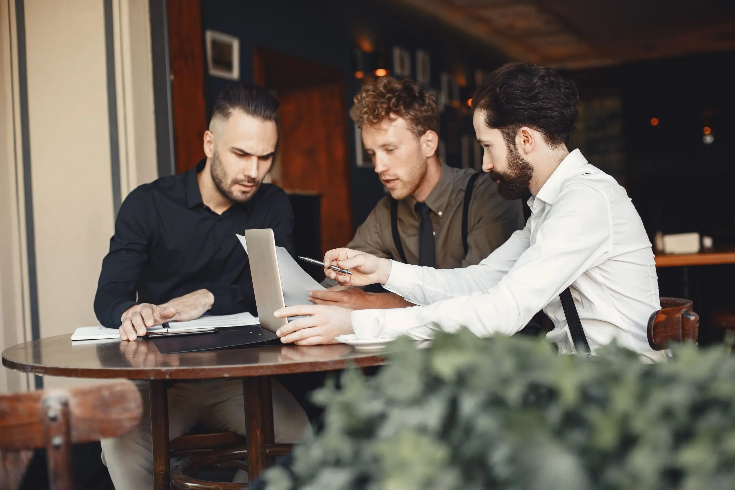 Tres hombres de negocios deliberando sobre documentos en un café