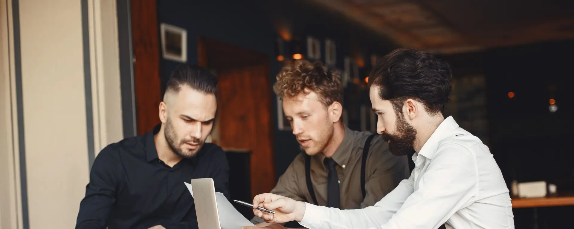Tres hombres de negocios deliberando sobre documentos en un café