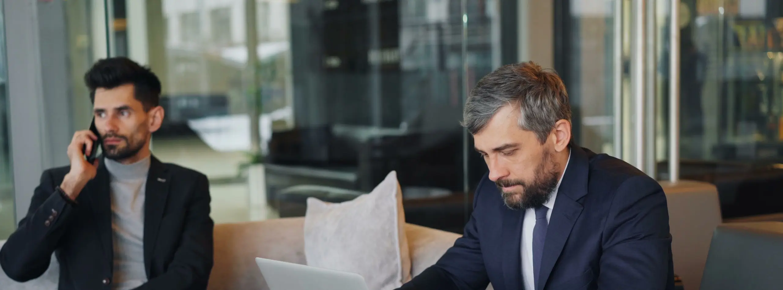 Dos hombres de negocios trabajando con portátil, café y documentos en un salón contemporáneo