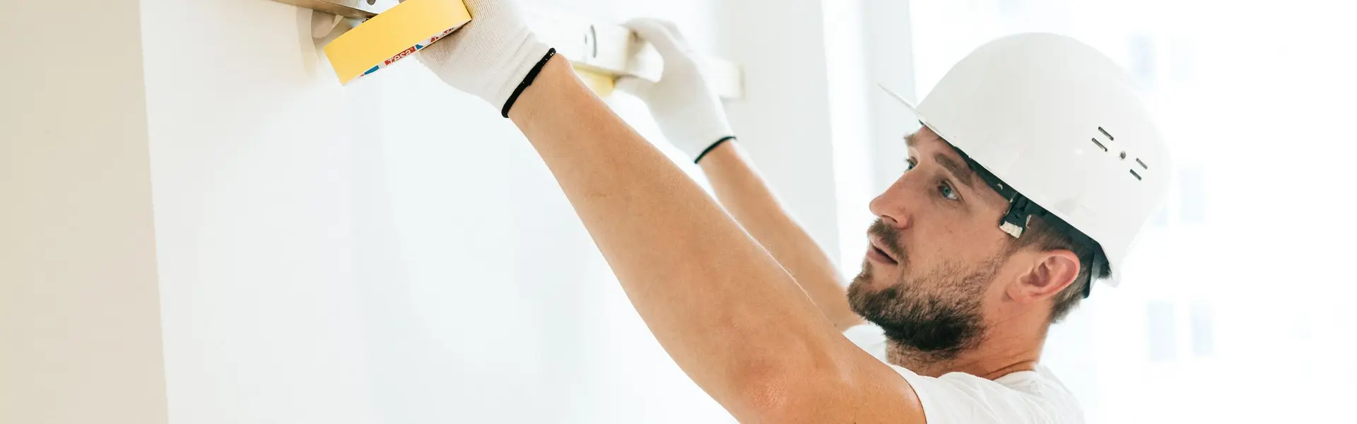 Albañil con casco blanco comprobando una pared recién acabada con el nivel de burbuja