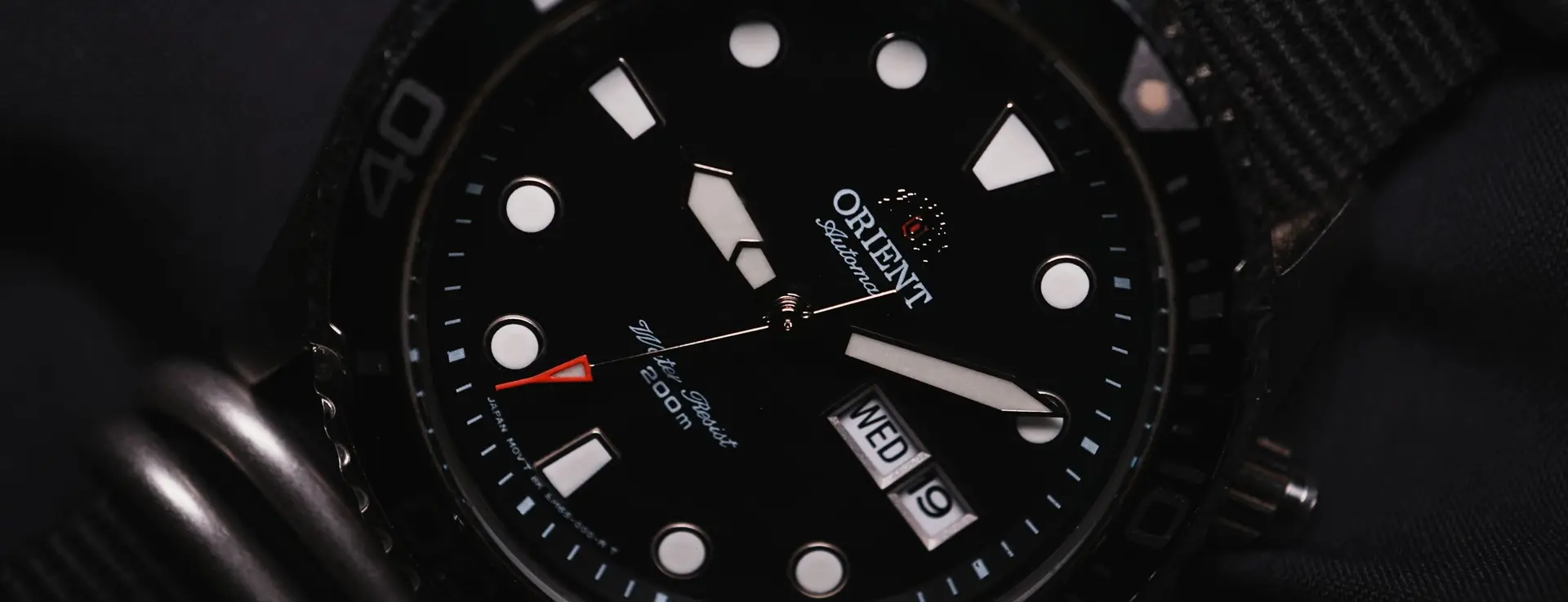 Reloj de buceo automático de esfera negra y bisel giratorio, con la leyenda «Water Resist 200m» en la esfera, sobre correa de tela