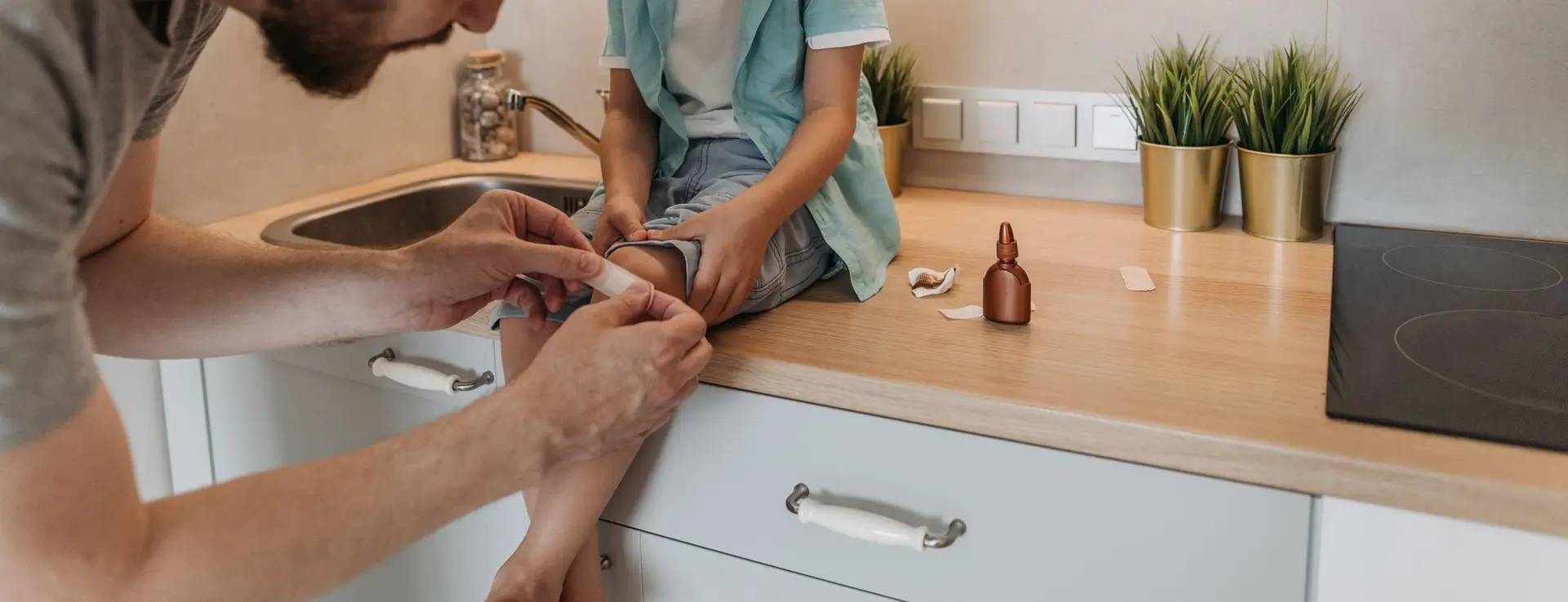 Un padre pone una tirita en la rodilla de su hijo, sentado en la encimera de la cocina
