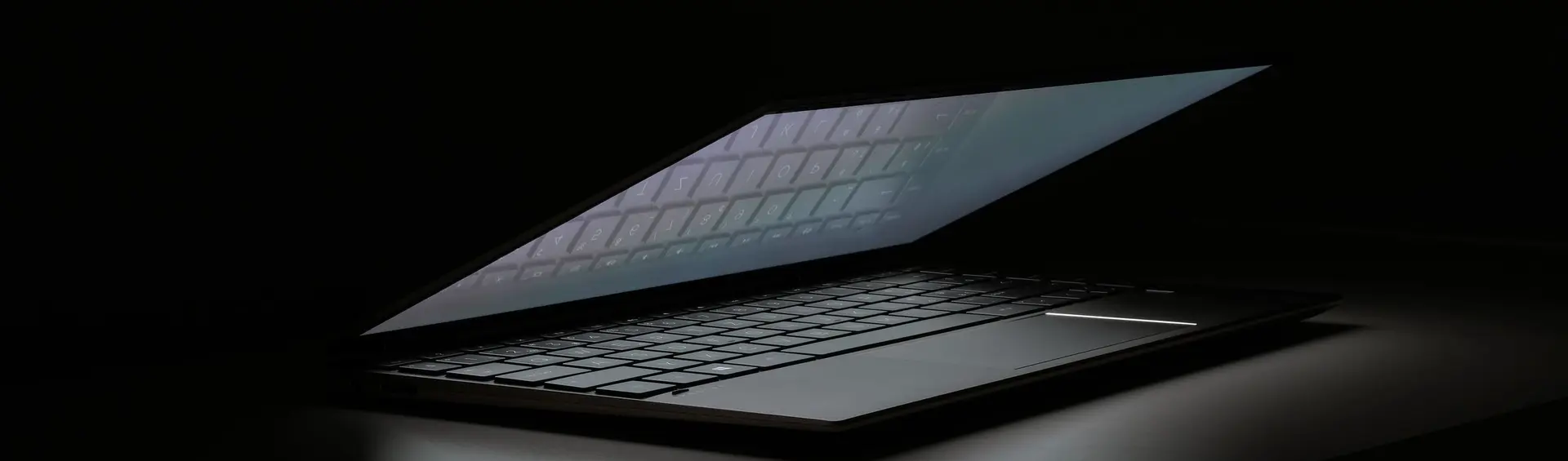 Portátil entreabierto a oscuras, con la luz de la pantalla escapando por la rendija sobre el teclado