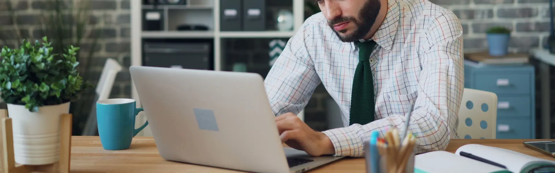 Hombre con camisa y corbata trabajando concentrado en un portátil sobre una mesa de madera