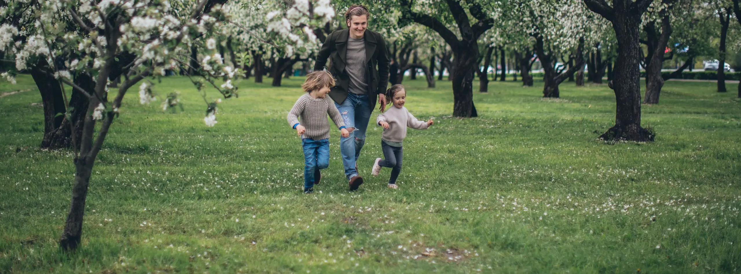Padre corriendo con sus dos hijos por un huerto de manzanos en flor