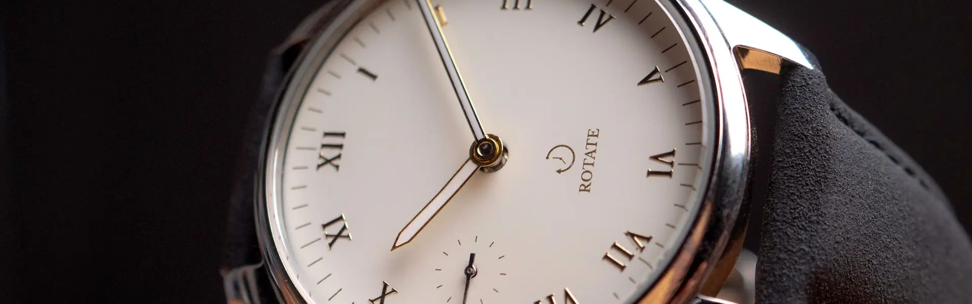 Reloj de vestir de esfera blanca con números romanos y pequeño segundero, sobre una peana de madera