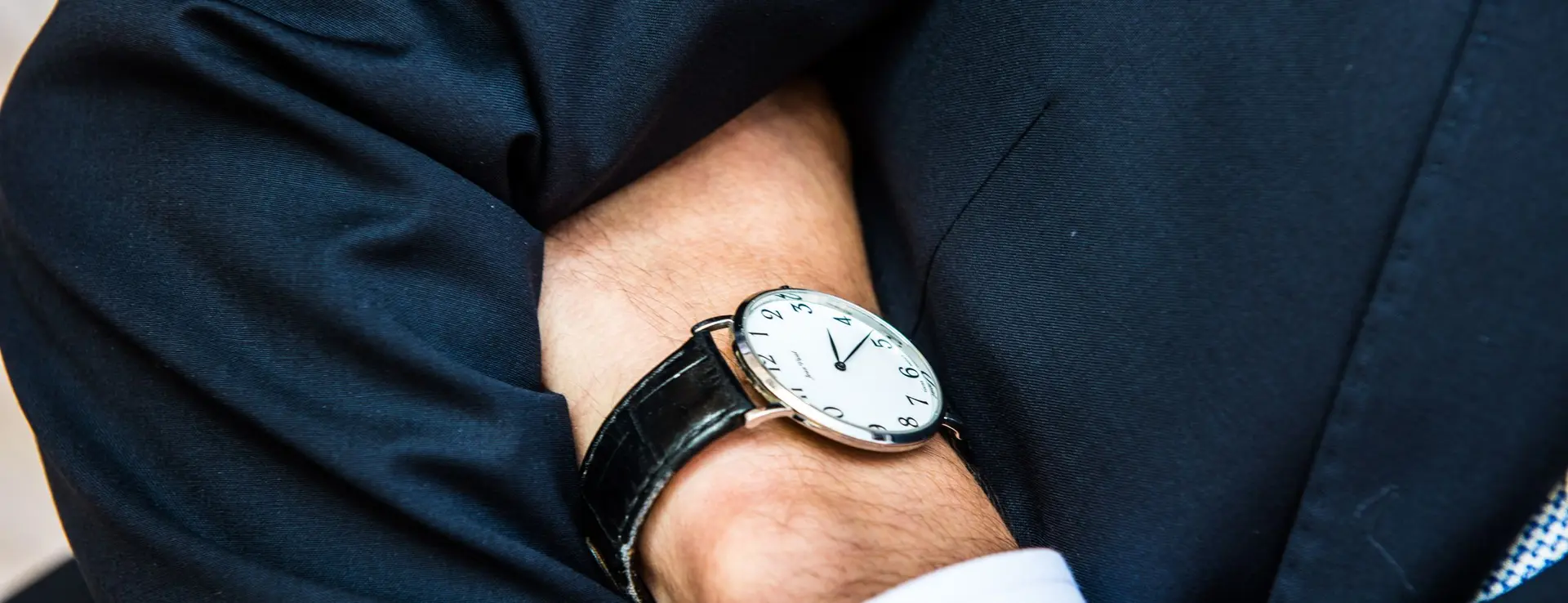 Muñeca de un hombre trajeado con un reloj de vestir de esfera blanca y correa negra