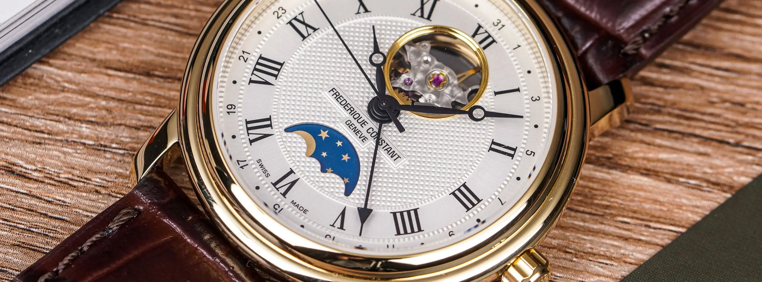 Reloj suizo dorado con esfera guilloché, fase lunar y correa de cuero marrón sobre una mesa de madera