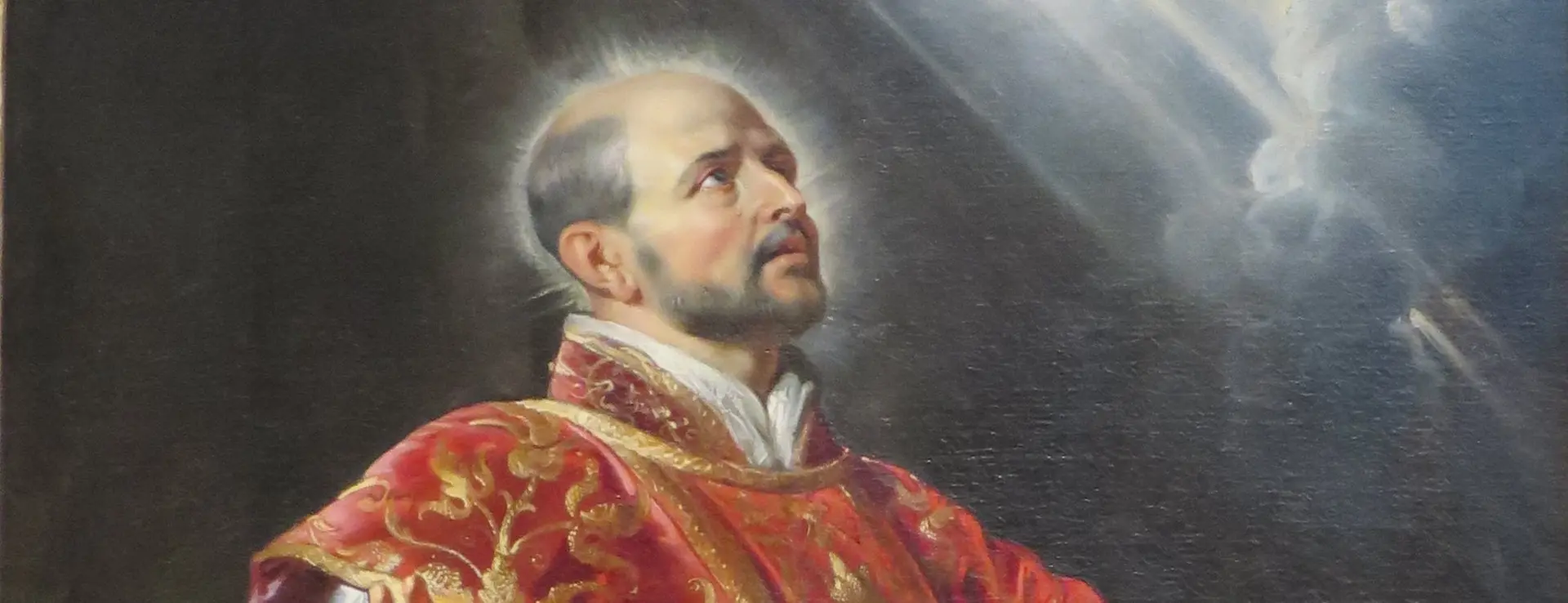 San Ignacio de Loyola, revestido de casulla roja y oro, alza los ojos a un rayo de luz con la mano sobre el libro donde se lee «Ad maiorem Dei gloriam»