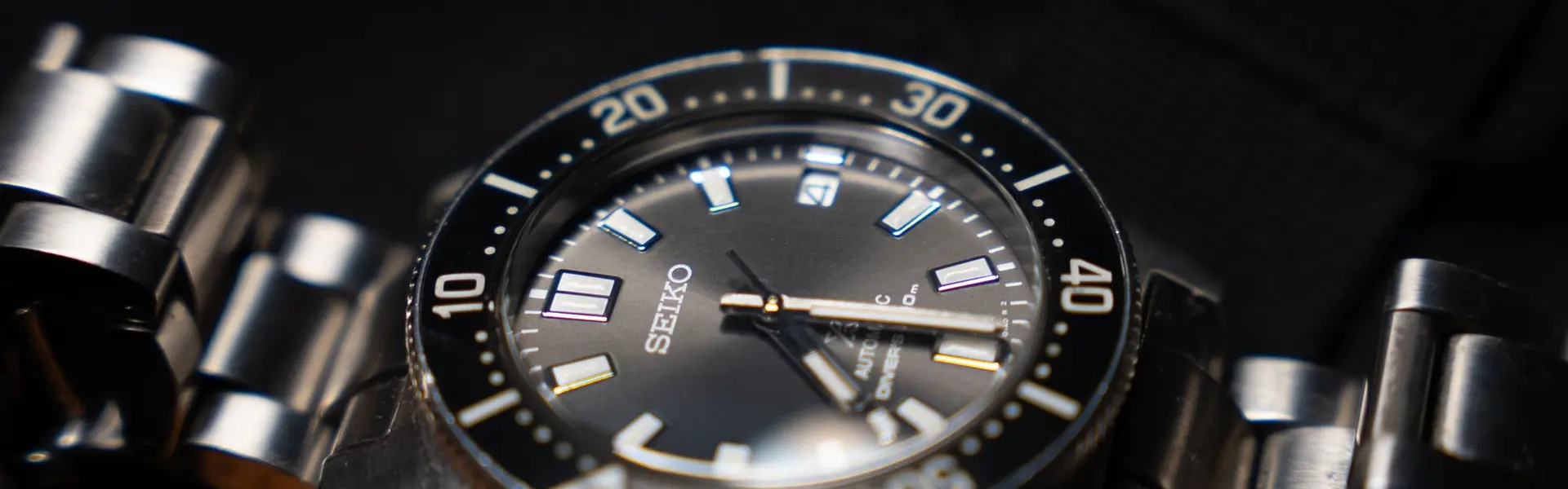 Reloj de buceo Seiko de esfera gris y bisel negro sobre brazalete de acero, en penumbra