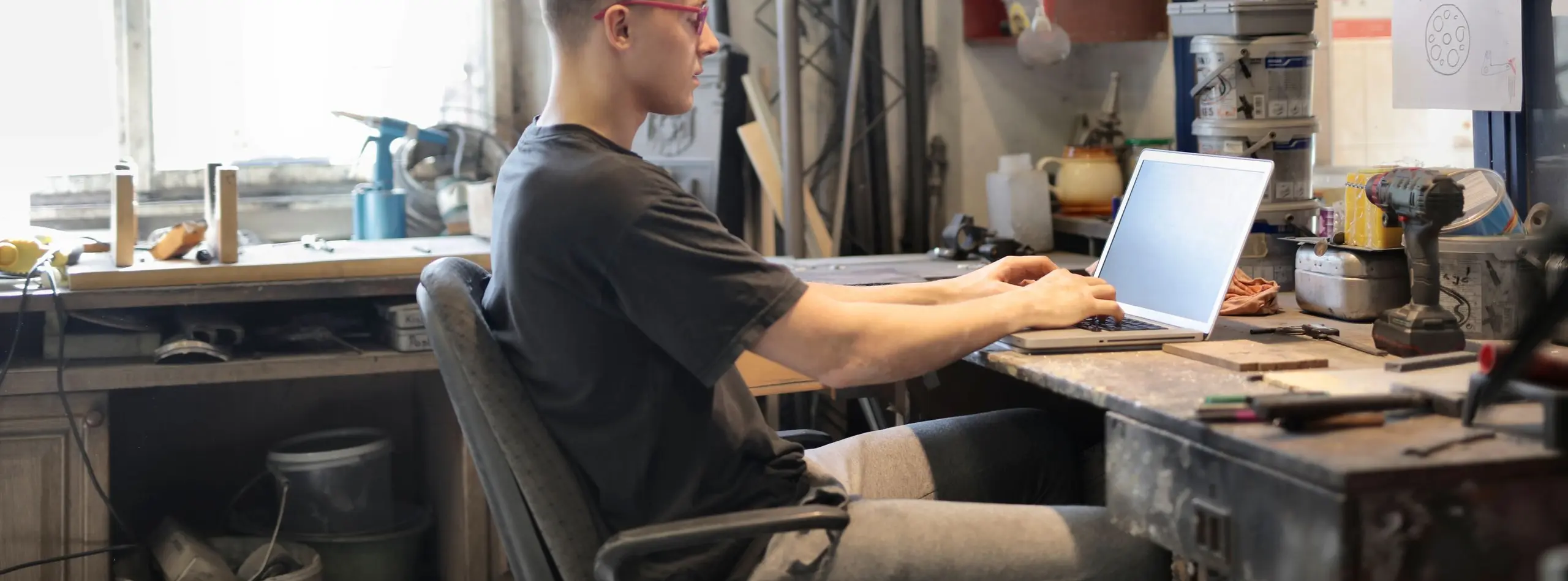 Joven trabajando con un portátil en un taller rodeado de herramientas