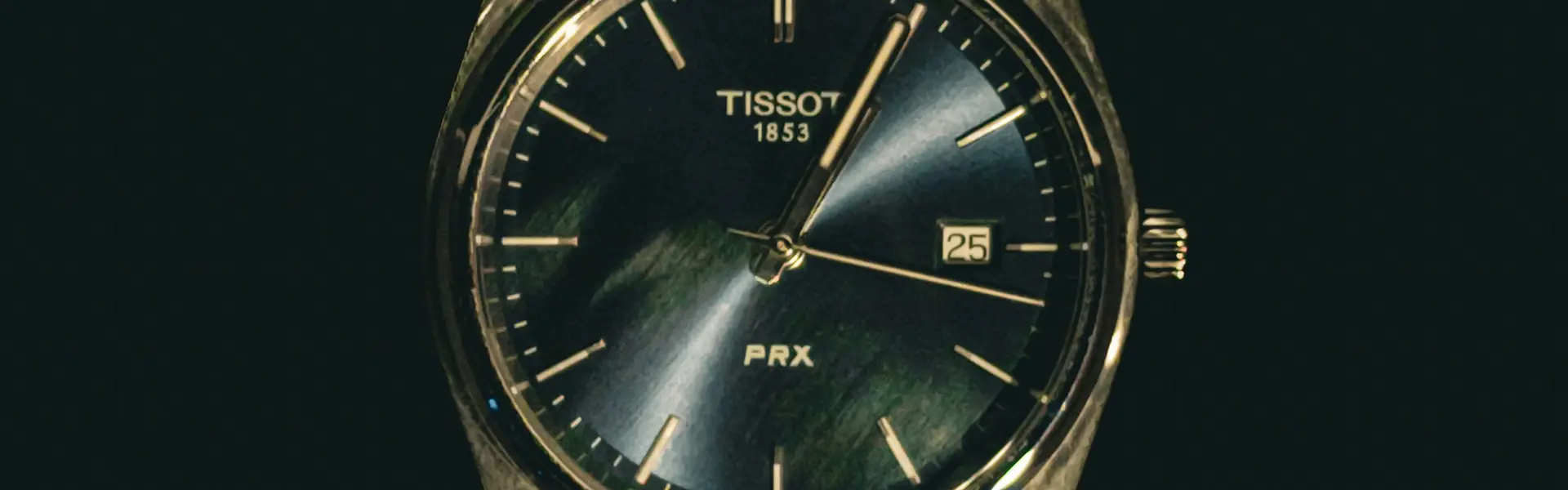 Tissot PRX de esfera oscura y brazalete integrado emergiendo de la penumbra